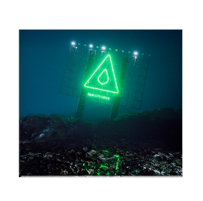 Image of the Rain city drive self titled album against a transparent background. neon green sign lit up at night, that says rain city drive. Above that is an image of a triangle with a raindrop in the center of it. The ground surrounding the sign is rocky.