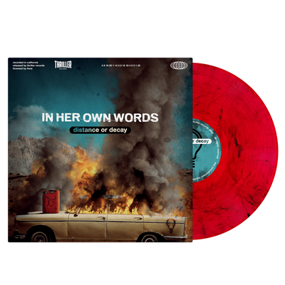 Image of a vinyl sleeve with a red and black smoke effect vinyl sticking out of the sleeve. The center of the sleeve says In her own words, distance or decay in white and transparent letters in the center. the album cover is an image of an old car with a gas can on the hood, the car windows and roof of the car up in flames. There are mountains in the distance and a blue sky above the car.