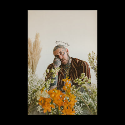Image of a poster against a transparent background. The poster features a photograph of riley- he is photographed from the mid section up. He is sitting and surrounded by orange, yellow, and white flowers. There is a halo above his head. The rest of the poster is white.