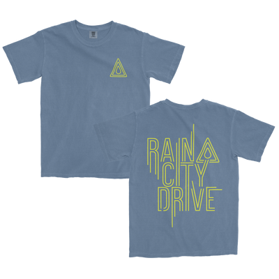image of the front and back of an indigo blue tshirt against a transparent background. The left chest has a yellow triangle on it, with a smaller yellow triangle inside of it and a raindrop in the center. The back of the shirt in yellow text says "rain city drive". The same logo from the front is next to the word Rain. Each word on the back of the shirt has its own line, so rain is at the top, then the word city below it, and drive below that.