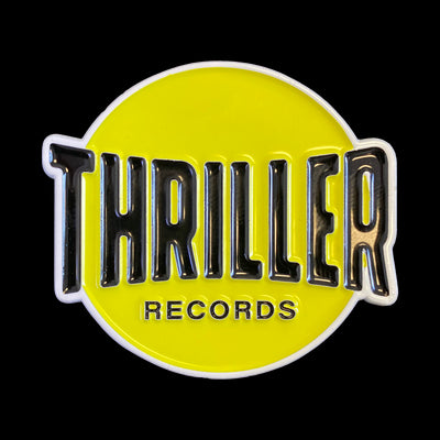 Image of the thriller records logo against a transparent background. The logo is a yellow filled circle outlined in white. in black text across it reads "thriller records". Thriller is in larger text, and records is in smaller text.
