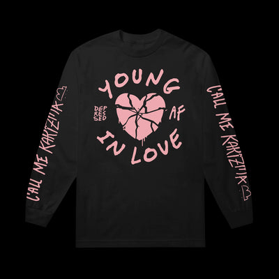 Image of a black longsleeve against a transparent background. The sleeves say Call Me karizma in pink text. There is a cloud next to the word karizma. The front design features a graphic of a heart that is broken. The shirt says young, in love, depressed af. The word young is above the heart, in love is at the bottom of the heart. The word depressed is to the left of the heart, and af is to the right of it.